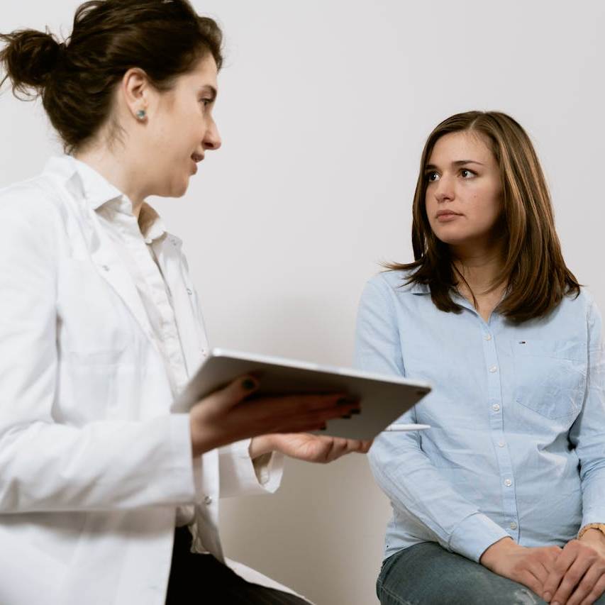 Eine Ärztin sitzt mit einem tablet in der Hand neben einer Patientin und spricht mit ihr.